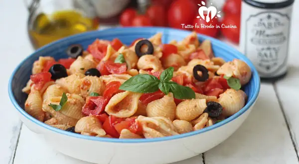 Un piatto di pasta con ricotta e pomodorini freschi, arricchito da olive nere e basilico.