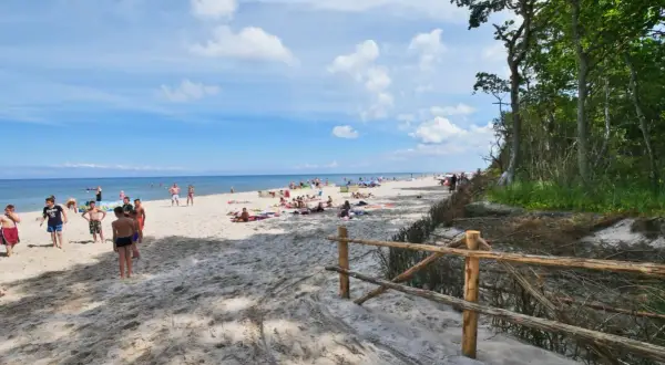 Słoneczny dzień na plaży w Karwieńskich Błotach. Ludzie odpoczywają na piasku, a morze spokojnie faluje.