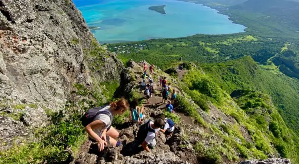 Wanderer erklimmen den Le Morne Brabant, eine atemberaubende Bergformation mit Blick auf das türkisfarbene Meer und üppige grüne Landschaften.