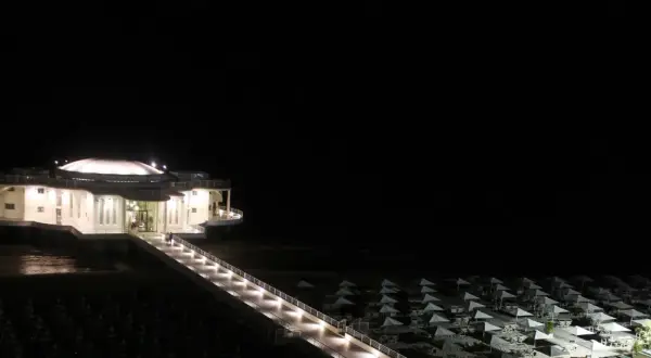 La Rotonda a Mare di Senigallia illuminata di notte, con la passerella che conduce all'edificio e la spiaggia con ombrelloni chiusi.