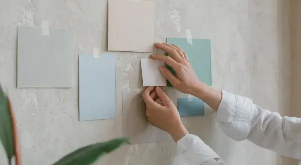 Händer arrangerar färgglada papper på en vägg. Tre tavlor bredvid varandra bildar en del av en moodboard.