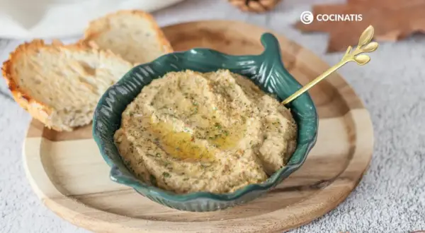 Delicioso pate de berenjena cremoso, servido en un cuenco verde con un toque de aceite de oliva y perejil. Acompañado de tostadas crujientes.