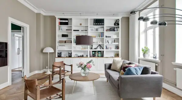Stilvolle wandgestaltung wohnzimmer mit einem weißen Bücherregal, Ledersesseln und einem grauen Sofa.