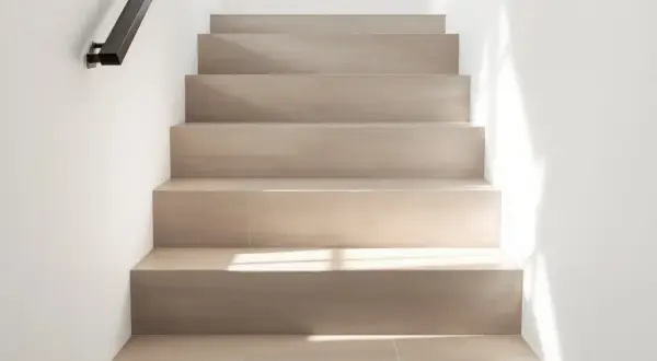 Escaliers en carrelage clair, sans joints apparents, avec un éclairage doux. On peut marcher sur du carrelage sans joint pour un look épuré.