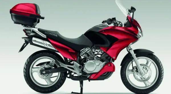 Czerwony motocykl Honda Varadero 125 z kufrem, gotowy na długie trasy. Silnik V-twin zapewnia niezawodność i dobrą żywotność.