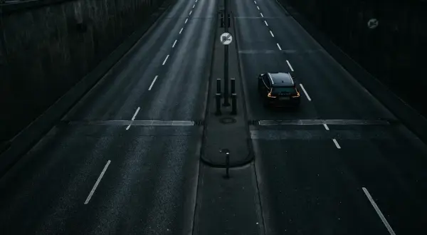 Czarny samochód na pustej, mokrej drodze asfaltowej z białymi pasami.