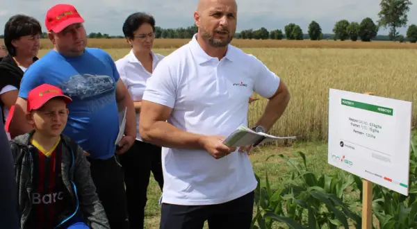 Grupa ludzi na polu kukurydzy, gdzie prezentowane są środki ochrony roślin, w tym metkonazol.