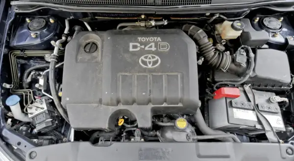Silnik D-4D w Toyocie Corolla E12. Widoczny jest plastikowy kolektor dolotowy, akumulator i inne elementy komory silnika.