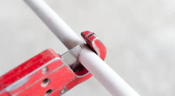 A red pipe cutter is shown in action, demonstrating how to cut PVC pipe cleanly and efficiently.