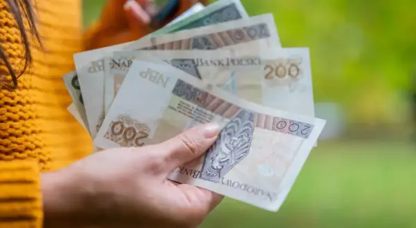 Dłoń trzyma polskie banknoty 200 zł. Zastanawiasz się, ile to netto po przekroczeniu drugiego progu podatkowego?