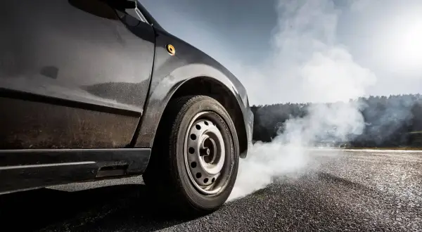 Une voiture freine brusquement, dégageant une épaisse fumée blanche. L'odeur de brûlé de plaquette de frein neuve emplit l'air.