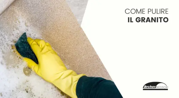 Mano con guanto giallo pulisce una superficie in granito con una spugna e schiuma.