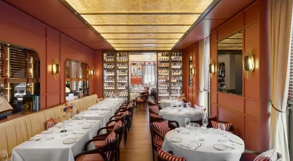Intérieur d'un restaurant typique Milan, tables dressées, murs corail, étagères à vin illuminées et plafond dorée.