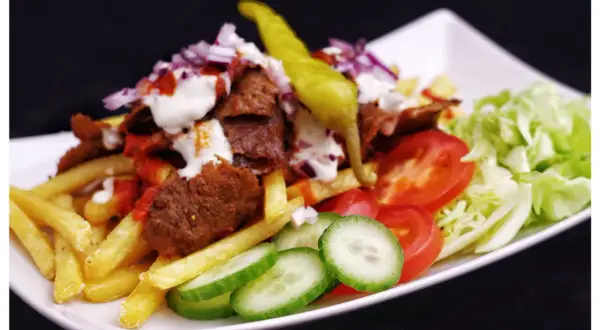 En tallrik med kebab, pommes frites, tomater, gurka, sallad och en grön chili. Perfekt för dig som söker ett gott kebabsås recept.
