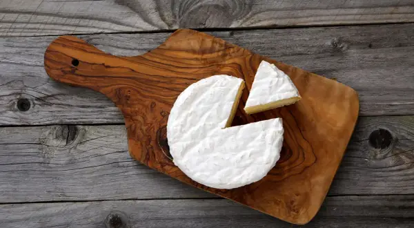 Un morceau de **brie** crémeux, avec une part coupée, sur une planche en bois rustique.
