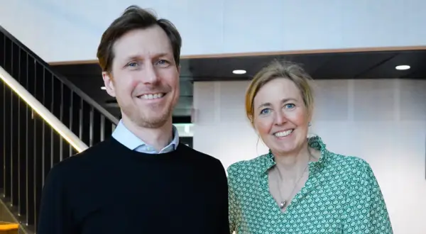 Tobias Sahlin ler glatt bredvid en kvinna i grön mönstrad blus. De står framför en trappa med belysning.
