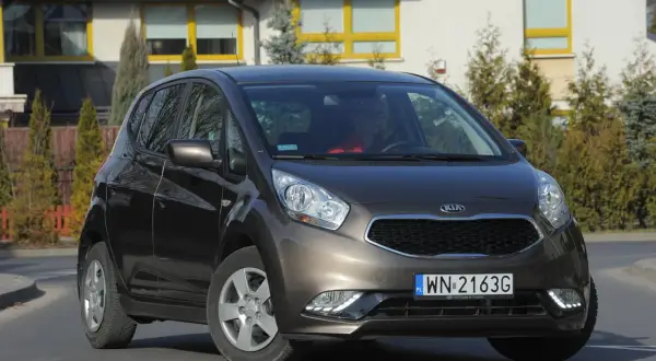 Brązowa Kia Venga z nowymi żarówkami LED, zaparkowana przed nowoczesnym domem.
