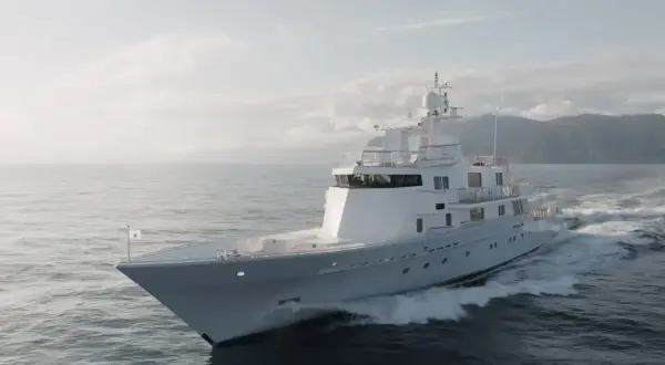 L'alessandro del bono yacht solca le onde con eleganza, un gioiello bianco su un mare calmo, con montagne sullo sfondo.