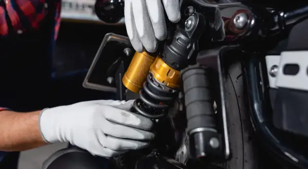 Mains gantées ajustant un amortisseur doré sur une moto. Faut-il changer les 4 amortisseurs pour une meilleure tenue de route ?