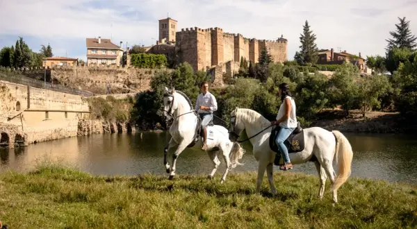 Paseo a caballo junto al río en Buitrago de Lozoya, con el castillo medieval al fondo.