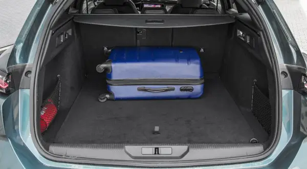 Bagażnik Peugeot 308 SW gotowy na wakacje. W środku niebieska walizka i apteczka.