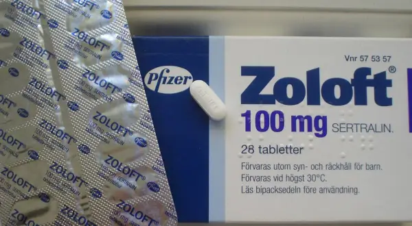 Opakowanie leku Zoloft 100 mg z sertraliną, obok blistra z tabletkami. Zoloft pomaga w leczeniu depresji.