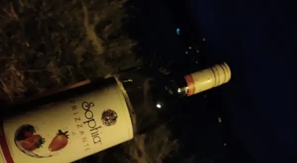 Butelka wina Sophia Frizzante z truskawkami na etykiecie, leżąca na ciemnym tle.