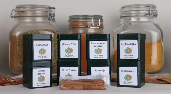 En samling mörkgröna burkar med kryddor, inklusive Garam Masala, som förbereder för en indisk kryddblandning.