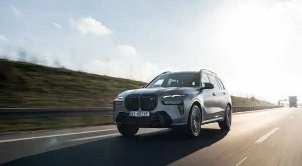 Szary BMW X7 M60i pędzi autostradą w słoneczny dzień.