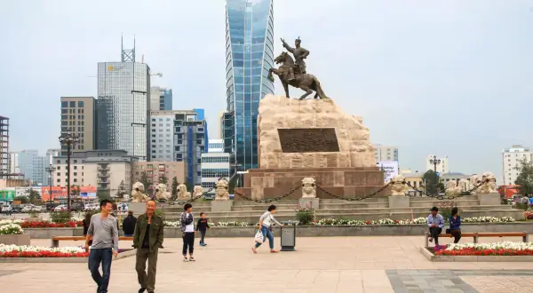 Pomnik Czyngis-chana na placu w Ułan Bator, stolicy Mongolii, z nowoczesnymi wieżowcami w tle.