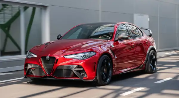 Czerwone Alfa Romeo Giulia GTAm z czarnym spojlerem i felgami pędzi po drodze.