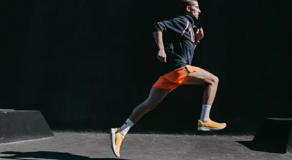 Mężczyzna w pomarańczowych spodenkach i żółtych butach biegnie dynamicznie. To inspiracja, jak przebiec 10 km.