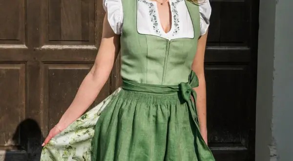 Tracht mit grünem Mieder und bestickter Bluse. Ein breiter Gürtel mit einer Schleife links betont die Taille.