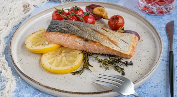 Gebratener Lachs mit Haut, serviert mit Zitronenscheiben, Kirschtomaten und Kräutern. Ein köstliches Rezept für Lachs mit Haut.