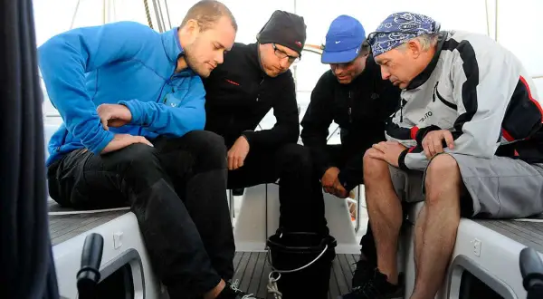 Vier Männer auf einem Boot, die sich über etwas beugen. Sie scheinen die Seefahrt zu genießen und haben ihre "sea legs" gut im Griff.