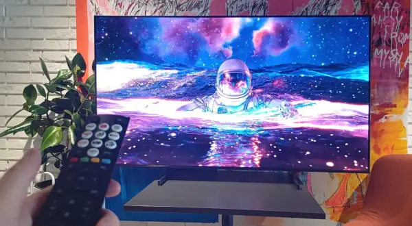 Telewizor wyświetla astronautę w kosmosie, trzymany jest pilot.