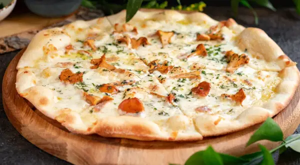 Pyszna pizza z kurkami, rozpływającym się serem i ziołami, podana na drewnianej desce.