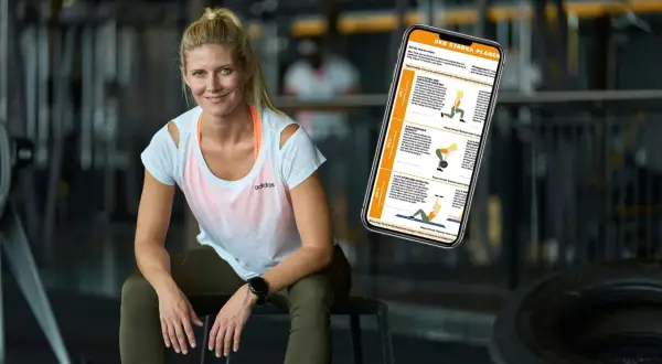 En kvinna sitter i ett gym med en telefon som visar en träningsplan. Hon ser ut att veta hur man blir stark.