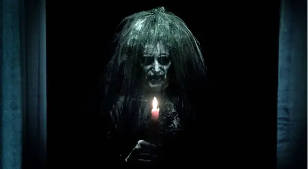 Przerażająca postać z zapaloną świecą, zapowiedź najstraszniejszych horrorów z jumpscare.