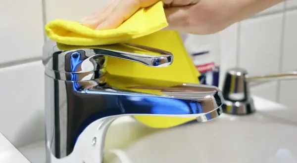Hand poliert glänzenden Wasserhahn mit gelbem Tuch. Der Wasserhahn geht schwer, aber die Reinigung macht ihn wieder leichtgängig.