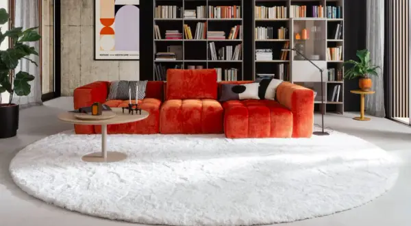 Ein flauschiger weißer Teppich bildet die Basis für das orangefarbene Sofa. So lässt sich der Teppich unter dem Sofa richtig platzieren.