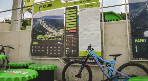 Mapa tras w bike parku Kasina z regulaminem i oznaczeniami trudności. Obok stoi rower enduro.