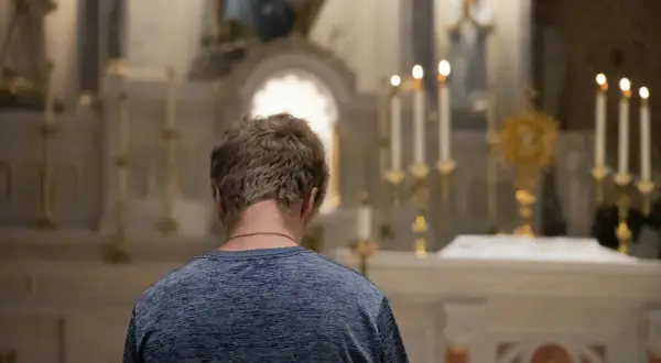 Młody mężczyzna klęczy przed ołtarzem, szukając rozgrzeszenia. Stosunek przerywany może być tematem jego modlitwy.
