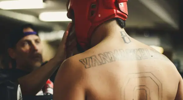 En fighter med röd hjälm och tatueringar på ryggen förbereds inför match. Kanske undrar du vad betyder MMA?