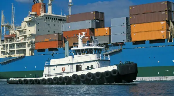Ein kleiner Schlepper assistiert einem riesigen Containerschiff. Der Unterschied zwischen vessel und ship wird hier deutlich.