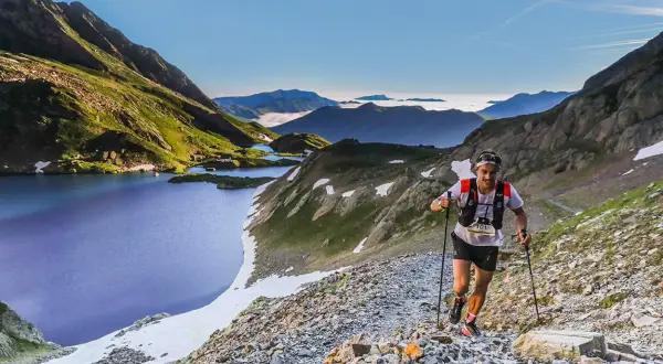 Un coureur de trail, le **vo2 max** à son apogée, grimpe un sentier rocailleux près de lacs de montagne bleus sous un ciel clair.