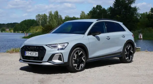 Jasnoszary Audi A3 allstreet stoi na żwirowej drodze nad jeziorem.