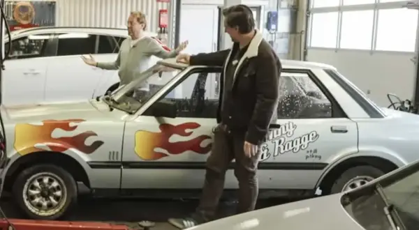 Två män vid en silverfärgad bil med flammor och texten "Ronny & Ragge".