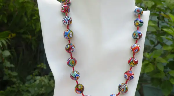 Colgantes de cristal de Murano, un collar vibrante con cuentas esféricas multicolores, cada una con un diseño floral único, sobre un fondo verde exuberante.