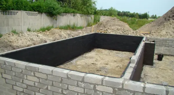 Fundament z bloczków betonowych, wewnątrz czarna izolacja. Widać kilka warstw bloczka fundamentowego.